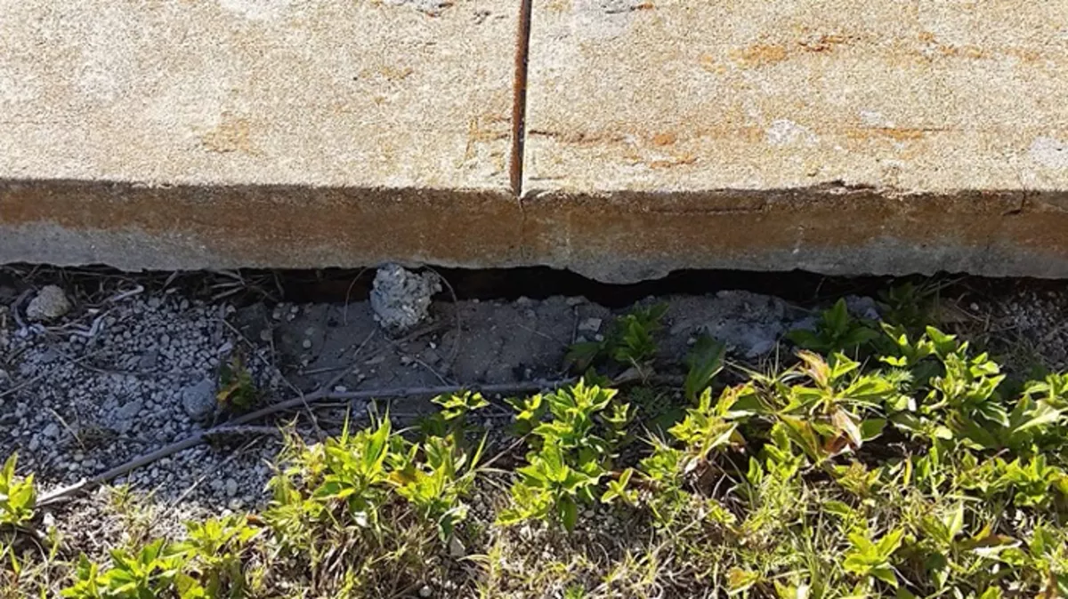 Visible gap beneath the edge of a concrete slab where soil has washed away